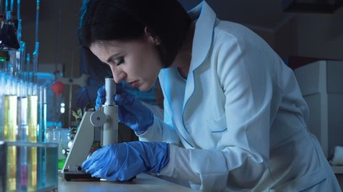Side view of woman in medical uniform looking at microscope in laboratory.
