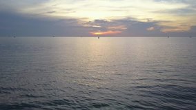 Flying over the sea into the sun and see fishing boat during sunrise by using a drone to take aerial footage

