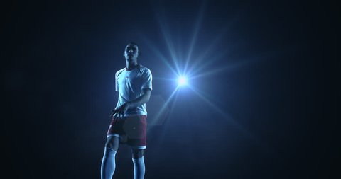 4K slow motion video of a male soccer player makes a dramatic play by jumping horizontally. He kicks the ball with his feet. The background is dark behind him. Only one of the lights shine brightly.