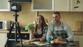 Young attractive couple bloggers shooting video food blog about cooking on dslr camera in the kitchen