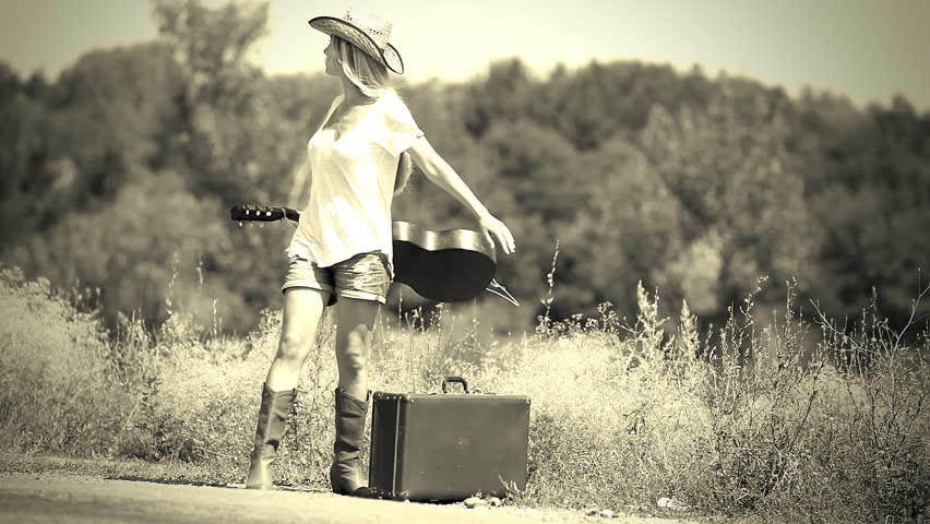 Young woman with guitar on the road and her vintage baggage