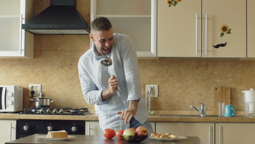 Slow motion of Attractive young funny man dancing and singing with ladle while cooking in the kitchen at home Royalty-Free Stock Footage #28508440