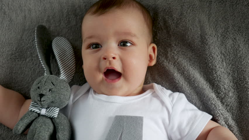 child in a white t-shirt bodysuit lying on her back and mom fun rattle multicolor plastic