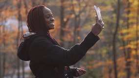 The side portrait of the smiling afro-american girl taking selfie in the autumn park.