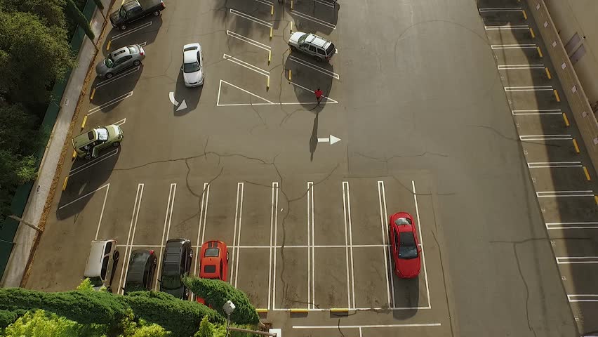 Aerial shot of parking lot, with man walking to his car and cars driving away.