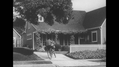 1950s: Paperboy rides bicycle into driveway. Paperboy throws newspaper onto house porch