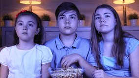 Group of children watching scary movie on TV in the evening at home
