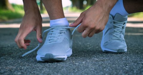 Athlete ties up shoelaces, white sneakers, white socks, in sports clothes, runs on the street. Concept: to love sports, a healthy lifestyle, to be beautiful, muscles, happy, strength and speed.