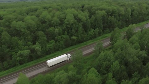 Semi Truck drives / traveling in forest asphalt road aerial footage / top view / Highway truck traffic