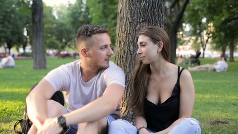 Guy with a girl talking in a park under a tree