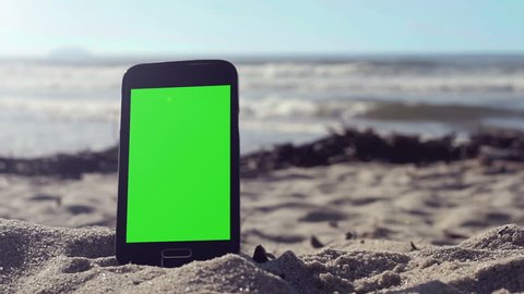 Generic black smart phone with green screen on the beach in Brazil, ready to key and replace.