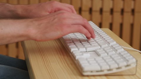 Close-up on a man typing on white keyboard on a wooden table. Filmed with studio light on a wooden background.