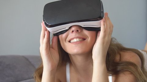 Young blonde woman playing game using VR-helmet for smart phones. Augmented reality device allows to deep into virtual space