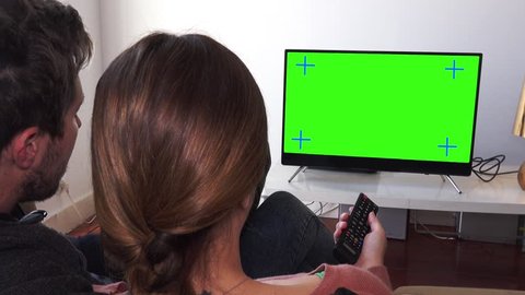 Couple Changing TV Channels Over Green Screen, Panning Shot. Couple watching television green screen relaxed at home. Pan camera behind models shoulders