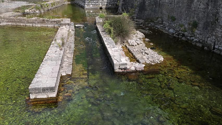 Fortress wall in Kotor Montenegro with moat. Green clear water in moat stream. Fortification from stones