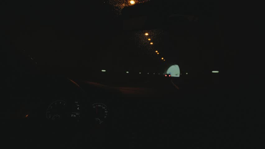 POV shot from inside hybrid car of woman behing steering wheel navigating through foggy dangerous mountain road at rainy day and drives in dark tunnels with lot of traffic.