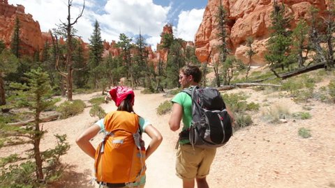 Hiking backpackers on hike in beautiful landscape in Bryce Canyon National park trekking smiling happy together. Multiracial couple, young Asian woman and Caucasian man in Utah, USA.