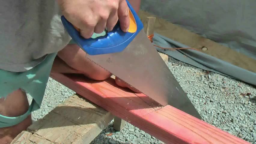 Carpenter cutting through framing timber with hand saw on home improvement