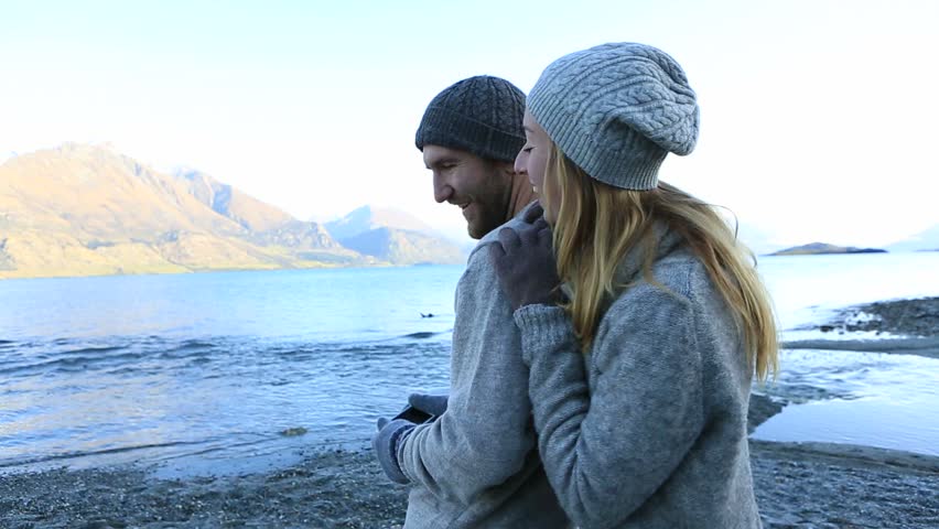 Young couple by the lake capture the mountain lake landscape on smart phone. Beautiful scenery in New Zealand.