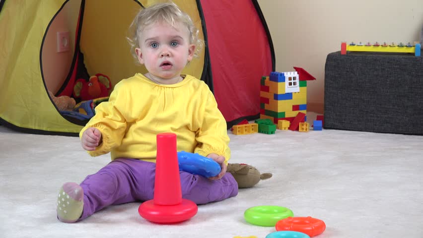 curly haired baby girl playing with colorful child pyramid. Child put circles on pole. Static closeup shot.