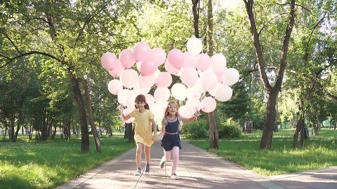 children run through the Park with a huge bunch of colorful balloons. two little girls with balloons on a background of green trees. slow motion