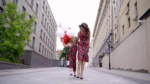 stylish couple of mom and her favorite daughter go model to walk through the street of the city in the fashionable clothes from designer. jumpsuit and dress with cherries.