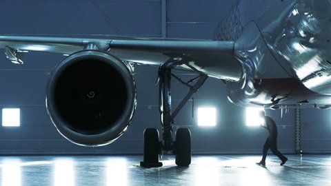 In a Hangar Aircraft Maintenance Engineer/ Technician/ Mechanic Inspects with a Flashlight Airplane's Jet Engine. Shot on RED EPIC-W 8K Helium Cinema Camera.