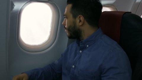 On a Transatlantic Flight Young Hispanic Male Opens Shade and Looks out of the Window. Shot on RED EPIC-W 8K Helium Cinema Camera.