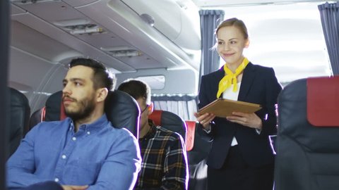 Airplane Stewardess/ Flight Attendant Shows Tablet Computer with Menu to Hispanic Male Passenger. They're Inflight. Business Class of a Commercial Aviation Interior is Visible. Shot on RED EPIC-W 8K 