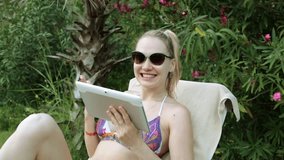 Beautiful woman in bikini talking on video communication. A girl in a swimsuit communicates using a tablet.