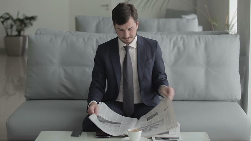 Young businessman is reading a newspaper and waits the boarding on the plane