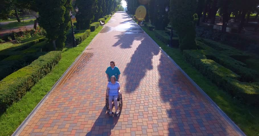Aerial footage of caregiver walking with disabled senior in wheelchair outdoors in park. 4k | Shutterstock HD Video #28632562