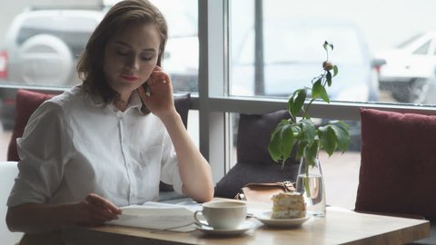 young business woman is resting during a lunch break at a cafe and leafing through women's fashion magazine