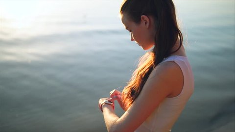 Woman touching smartwatch on beach during sunset. Female using smart watch app outdoors near the sea.
