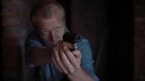 Security guard appears in an dark abandoned building with a gun and aiming at the camera.