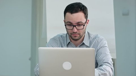 Handsome male teacher in glasses typing on laptop