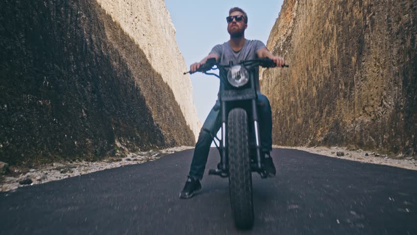 Motorcyclist driving his motorbike Between two rocks on the ocean beach