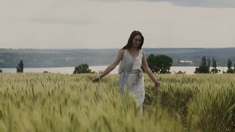 Young girl in the white dress is running through the field of wheat
