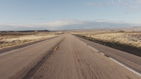 Driving USA: The open road – beautiful point of view shot driving on long straight road in desert grasslands at sunrise/sunset, Wyoming