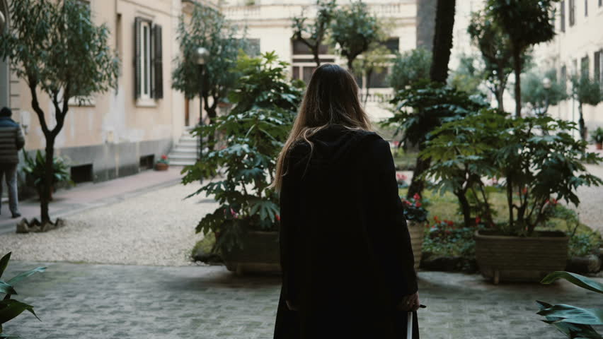 Back view of the young attractive woman with suitcase walking on the street. Female wearing black are coming in new city