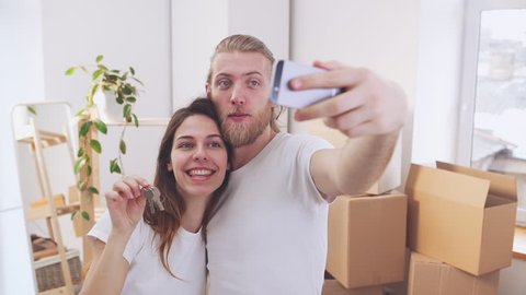 Happy smiling Caucasian pair making selfie and posing with keys from new home in slowmotion. Concept of happiness and life