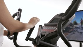 Woman using a smartwatch to monitor her progress during cardio workout on an elliptical trainer in front of the TV