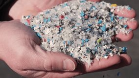 Slow motion close up video featuring a man's hands showing a handful of pieces of recycled plastic.