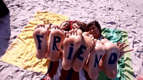 Word friends on the feet of young women lying at the beach. Footage of female friends at the beach with feet up and enjoying summer holidays.