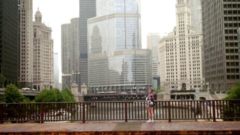 Happy smiling woman standing on bridge over river in big city and waving. Young beautiful woman stand on bridge. City buildings. Chicago city skyline
