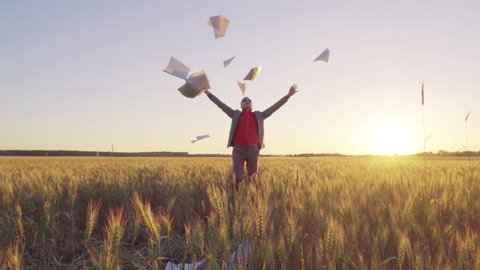 Businessman in a suit on a wheat field throws a stack of documents up and triumphantly throws up his hands, slow motion