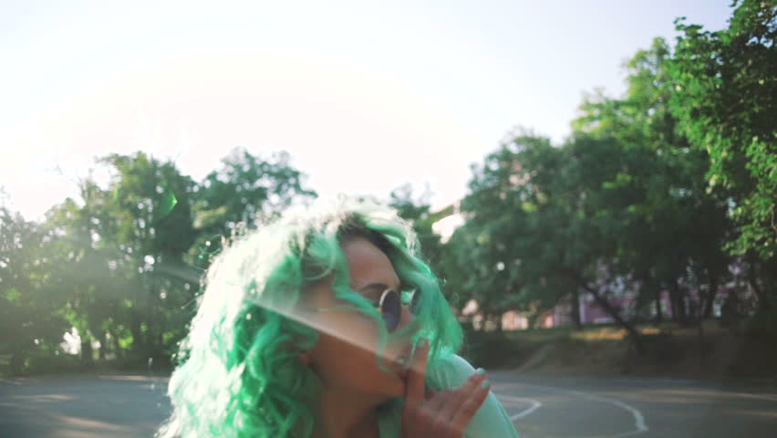 young stylish funky girl with green hair and sun glasses dancing outdoor, slow motion