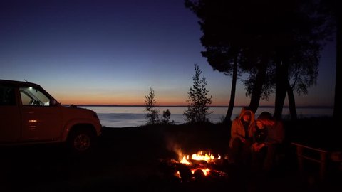Family of tree around a campfire at night with car. Lake on background