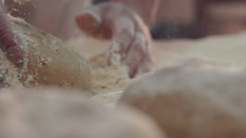Extreme close up view of baker’s hands one by one kneading the pieces of dough in the flour on the table. Beautiful process, daily routine. Baking manufacture, traditions. Bread-making industry.