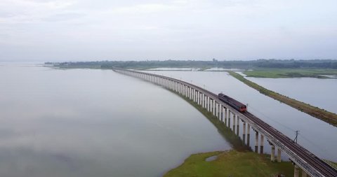 Amazing aerial view following passenger train runs on a floating railway bridge during morning with misty across the lake of Pa Sak Jolasid dam in Lopburi unseen Thailand.